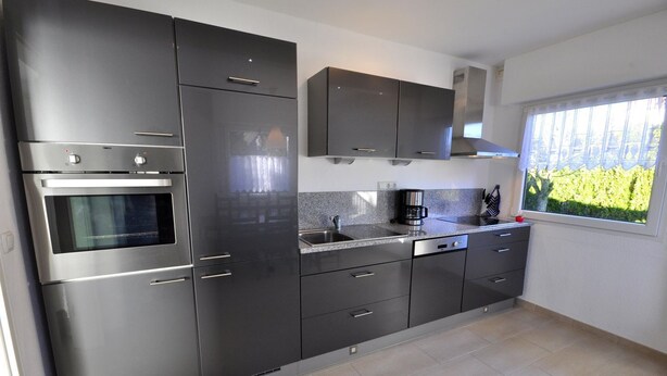 A modern kitchen with stainless steel appliances, a built-in oven, a coffee maker, and a window with a view of greenery.