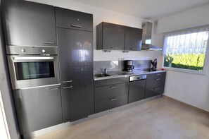 A modern kitchen with stainless steel appliances, a built-in oven, a coffee maker, and a window with a view of greenery. - "Up de Ring 13" Vacation Rental (Wittmund)