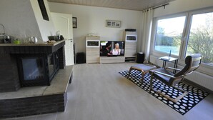 A modern living room with a fireplace, a television, and a large window offering a view of the outdoors.