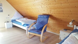 Ein Schlafzimmer mit Holzboden, einem Bett mit blauer Bettwäsche, einem blau gepolsterten Sessel und einem Nachttisch mit einer Lampe.