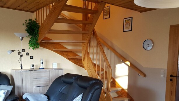 Ein gemütliches Zimmer mit einer schwarzen Ledersofa, einer Holztreppe, einem Schreibtisch mit Lampe und einer Uhr an der Wand.