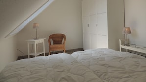 Een slaapkamer met een groot bed, een stoel, een kledingkast en twee nachtkastjes met lampen.