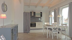 Une cuisine moderne équipée d’un four, un coin repas avec une table et des chaises, une horloge au mur et une lampe sur une table d’appoint.