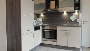 Une cuisine moderne avec des meubles blancs, un four encastré, une machine à café et un revêtement mural décoratif à motifs géométriques.