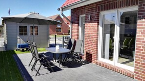 A patio with a table and chairs, a small shelter, and a brick building with large windows.