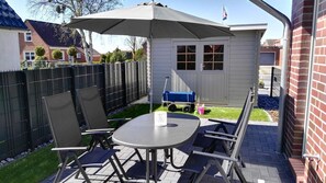 Une terrasse extérieure avec une table et des chaises, un parasol et un abri de jardin en arrière-plan.