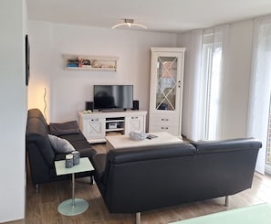 Ein modernes Wohnzimmer mit Flachbildfernseher, einer Couch, einem Couchtisch und einer Vitrine.