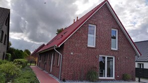 Une maison en briques rouges, avec un toit en pente, un numéro « 5 » bien visible sur la façade et un petit jardin.