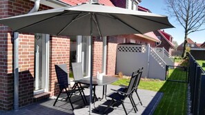 Une terrasse extérieure avec une table et des chaises, un grand parasol, et une maison en briques en arrière-plan.