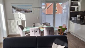 A modern living room with a black leather sofa, a dining area with a glass table, and a kitchen with white cabinets.