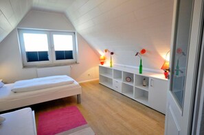 Ein kleiner, gut beleuchteter Raum mit schrägem Dach, einem Bett, einem Fenster und einer eingebauten Regaleinheit mit Dekorationselementen.