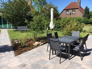 Eine Terrasse im Freien mit Tisch und Stühlen, einer Bank und einer kleinen Gartenanlage mit Steinen und Pflanzen.