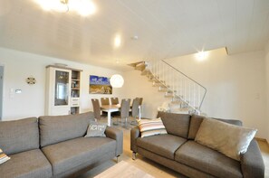 Ein modernes Wohnzimmer mit zwei Sofas, einem Esstisch mit Stühlen und einer Treppe.