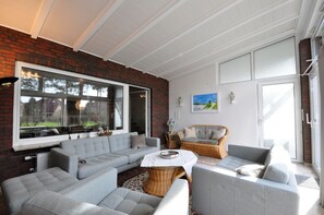 Ein modernes Wohnzimmer mit einem grauen Ecksofa, einem Korbsessel und einem kleinen Tisch.