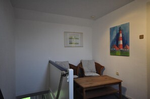 A small room with a wooden bench, a chair, a framed picture on the wall, and a painting of a lighthouse. - Vacation home Mühlenstraße 12 Nr. 1 - Holiday home Mühlenstraße 12 Nr. 1 in (Wittmund)