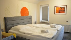 A neatly made bed with white linens and towels, a grey upholstered headboard, and a window with blinds. - Vacation home Mühlenstraße 12 Nr. 1 - Holiday home Mühlenstraße 12 Nr. 1 in (Wittmund)