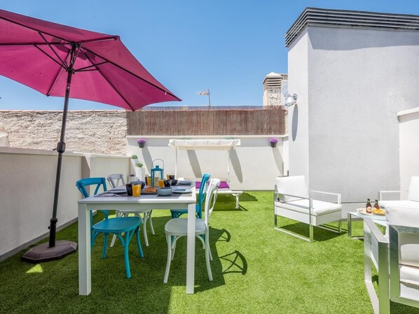 Eine Dachterrasse mit Tisch für zwei Personen, einem großen Sonnenschirm und Sitzgelegenheiten im Freien.