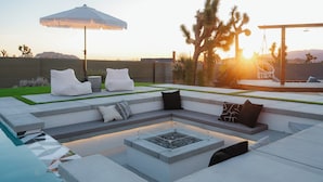A modern outdoor seating area with a pool, cushioned seating, and a pergola. - Ventana Cove Pickleball and Saltwater Pool (Yucca Valley)