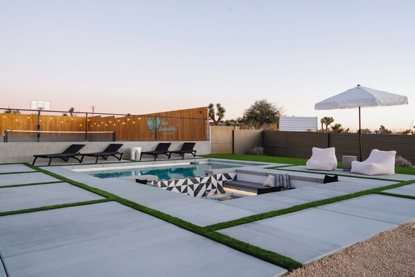 Un patio trasero con piscina, sillas de descanso y una sombrilla blanca.