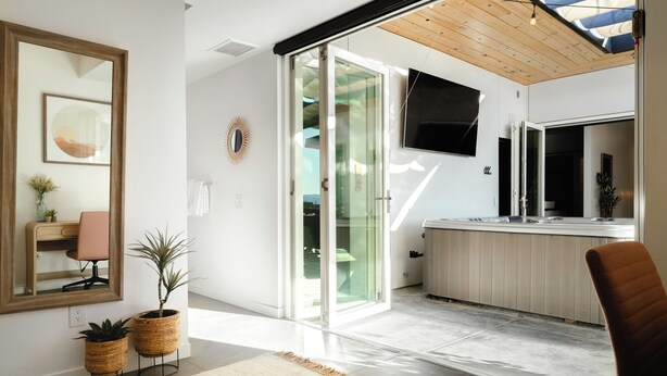 A modern kitchen with a large island, sliding glass doors leading to a balcony, and a flat-screen TV mounted above the island. - Ventana Cove Pickleball and Saltwater Pool (Yucca Valley)