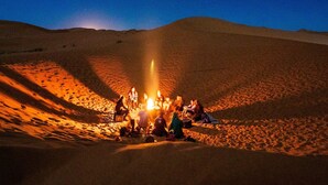 A group of people gathered around a campfire in a desert setting. - Camel trek bivouac in Merzouga (Merzouga)