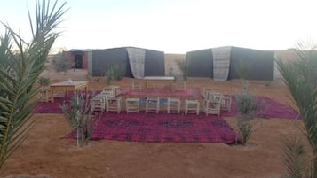 A desert setting with a seating area featuring wooden furniture and a red carpet.