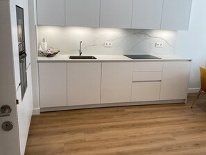 Une cuisine moderne avec des meubles blancs, un évier à deux bacs et un dosseret en marbre.