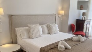 A neatly made bed with pillows, a bedside table, a chair, and a lamp.