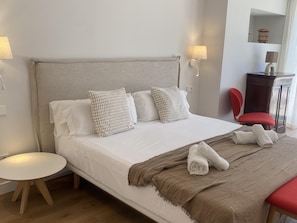 A neatly made bed with pillows, a bedside table, a chair, and a lamp.