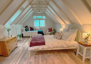 Ett sovrum med ett sluttande tak, en säng med många kuddar, ett sängbord med en lampa och en byrå.