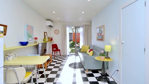 A compact living space with a checkered floor, a sofa, a dining table, and a small kitchen area.