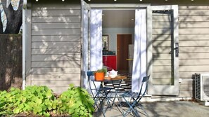 En täckt uteplats med ett bord och stolar, en krukväxt och ett litet bord med en tekanna.