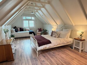 Une chambre à coucher aménagée dans un espace mansardé, avec un plafond en pente, un lit, un coin salon et une fenêtre offrant une vue.