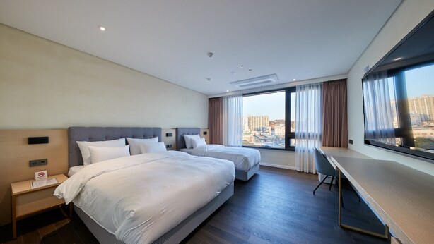 Habitación de hotel con dos camas, un escritorio y un ventanal amplio con vistas a la ciudad.