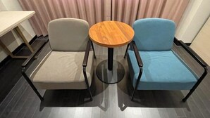Una habitación con una mesa redonda de madera, dos sillas, una color beige y otra azul, y una mesita a la izquierda.