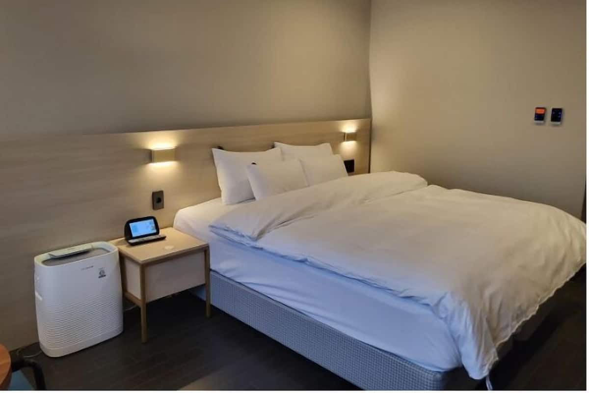 Ein modernes Hotelzimmer mit einem großen Bett, einem Nachttisch mit Lampe und einem kleinen Luftreiniger.