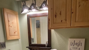 Une salle de bain avec des meubles en bois, un lavabo blanc, un miroir, des toilettes et un panneau indiquant : « Lavez-vous les mains ».