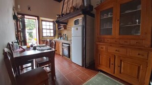 Una cocina con armarios de madera, una mesa de comedor, sillas, un refrigerador y un ventanal.