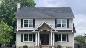 A two-story house with a central entrance, a brick foundation, and a dark roof. - Modern Cheerful Bluegrass Beauty (Lexington)