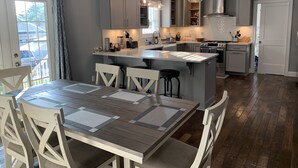 A modern kitchen with grey cabinets, a central island, pendant lighting, and a dining area with a table and chairs. - Modern Cheerful Bluegrass Beauty (Lexington)