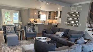 A modern living room with grey sofas, a coffee table, and a dining area with a kitchen in the background. - Modern Cheerful Bluegrass Beauty (Lexington)