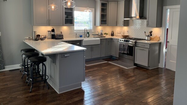 A modern kitchen with grey cabinets, a central island with bar stools, a built-in oven, and pendant lighting. - Modern Cheerful Bluegrass Beauty (Lexington)