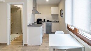 A compact kitchen with a dishwasher, microwave, and a small island. There's a dining area with a table and chairs, and a shower area with glass doors. - Housing León Azabachería 2A (León)