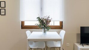 A white dining table with two chairs, a vase with flowers, and a TV on a stand. - Housing León Azabachería 2A (León)
