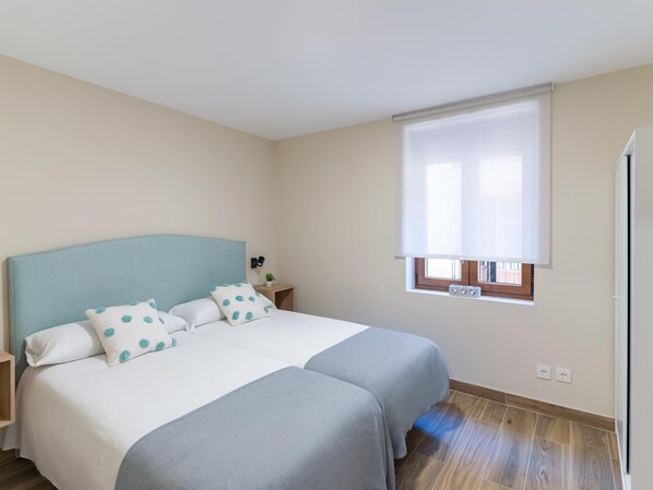 A bedroom with a bed, bedside tables, a window with blinds, and a wooden floor.