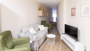A modern living room with a grey sofa, green armchairs, a white round side table, and a flat-screen TV on a white stand. - Housing León- Azabachería 1B (León)