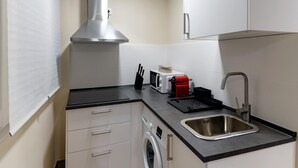 A compact kitchen with a stainless steel range hood, a microwave, a red coffee maker, a sink, and a washing machine. - Housing León- Azabachería 1B (León)
