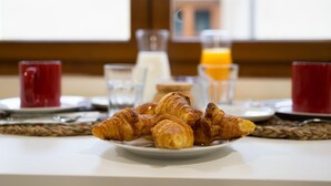 A breakfast setting with croissants on a plate, a glass of orange juice, and a glass of milk. - Housing León- Azabachería 1B (León)