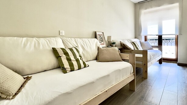 Una sala moderna con un sofá, una cama de madera y un balcón con barandilla.