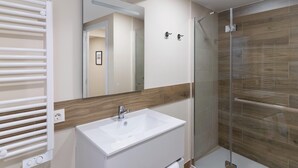 Un baño moderno con lavamanos blanco, cabina de ducha de vidrio y pared de acento de madera.